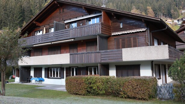 Eine mehrstöckige Holzhütte mit Balkonen, einer Veranda und Blick auf einen bewaldeten Berg.