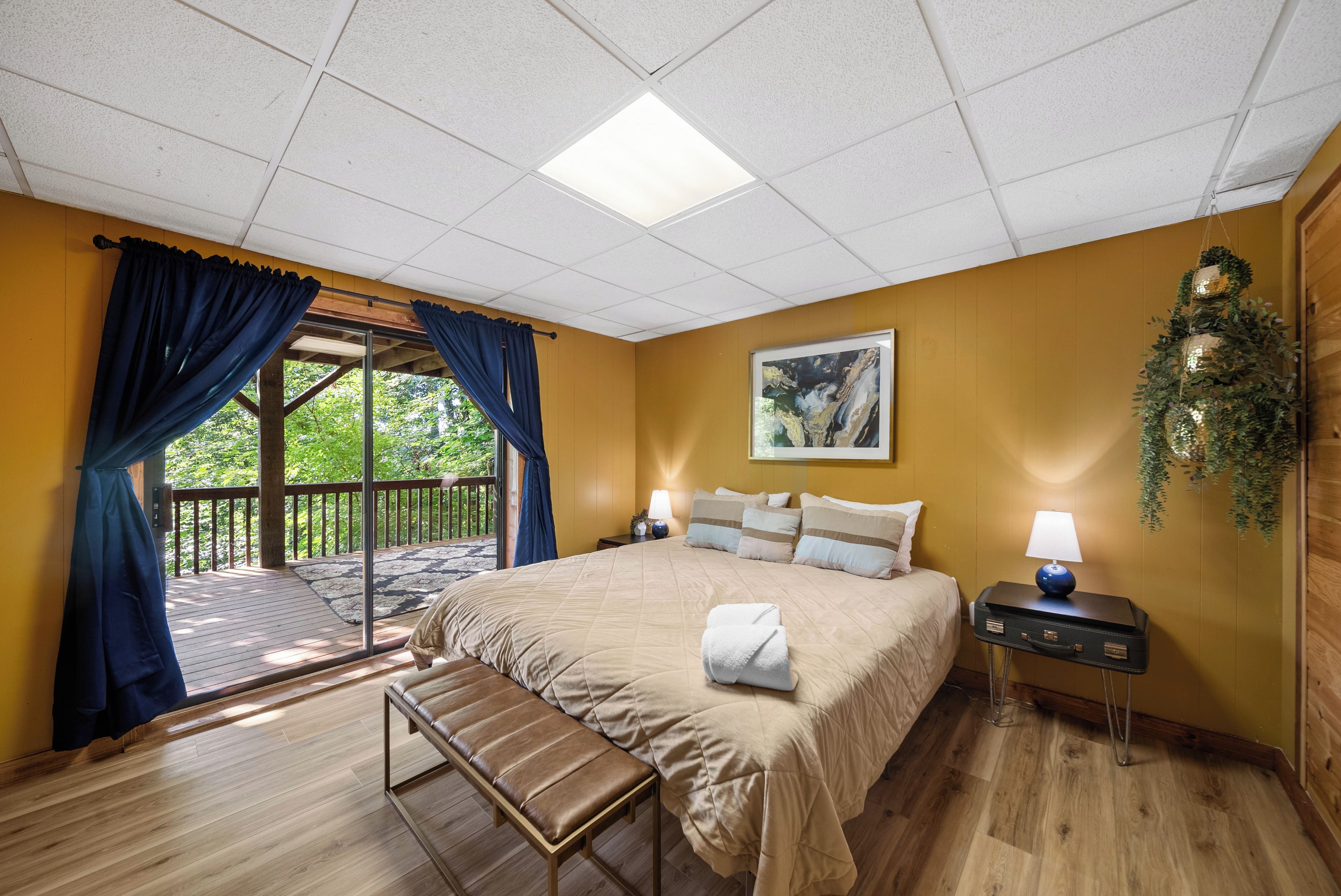 Une chambre d’hôtel avec un grand lit, une banquette, une table de chevet, une lampe et une vue sur l’extérieur.