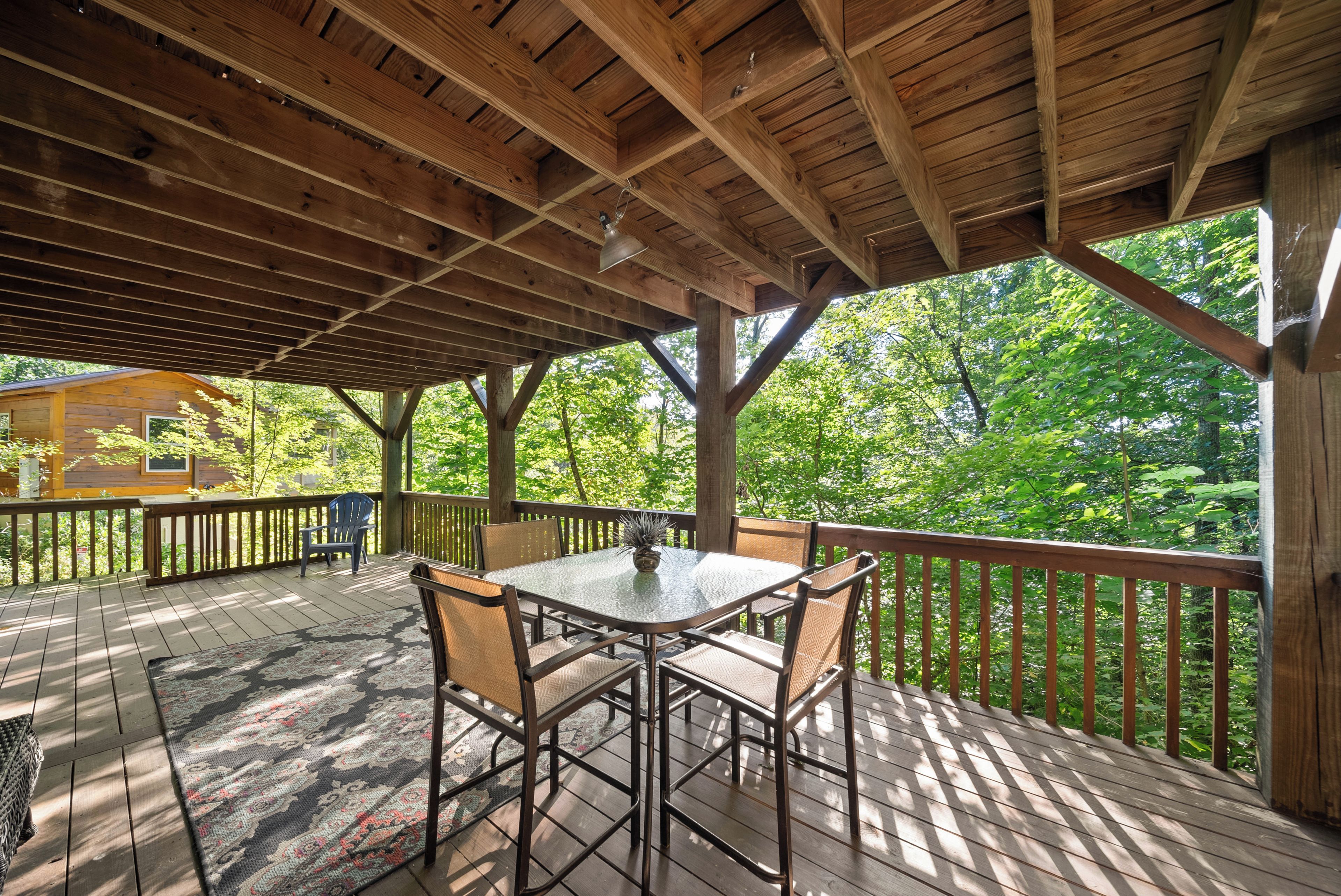 A covered outdoor deck with a table and chairs, surrounded by a wooden railing.