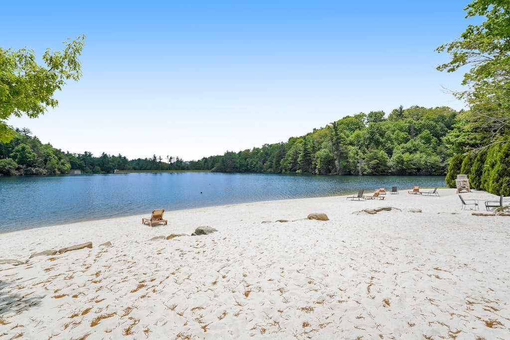 A beach with clear water, surrounded by trees, and includes several lounge chairs.