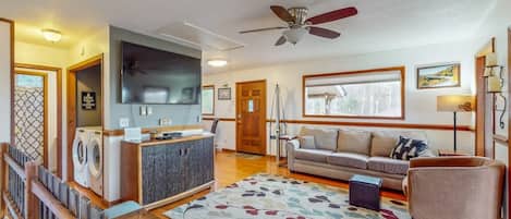 A living room with a sofa, a television, a ceiling fan, and a washing machine.