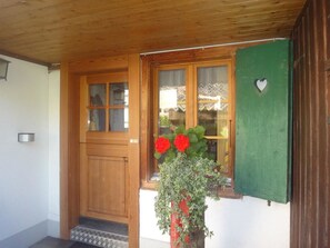 Une porte en bois avec un panneau de verre, un auvent vert et un pot de fleurs contenant des fleurs rouges.