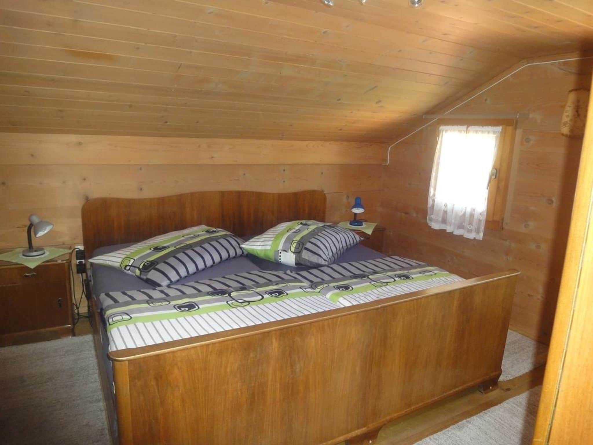 A wooden cabin bedroom with a single bed, a nightstand, a lamp, and a window with curtains.