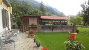 Un pati amb taula i cadires, una estructura de fusta amb teulada vermella i un jardí ben cuidat.
