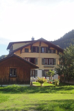 Ein zweistöckiges Gebäude mit einem Holzbau auf der linken Seite und einer gelben Fassade auf der rechten Seite.