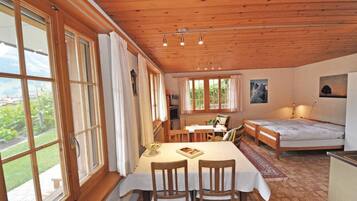Une pièce chaleureuse avec un plafond en bois, de grandes fenêtres, une table à manger avec des chaises, un canapé et un lit.