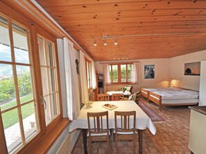 A cozy room with a wooden ceiling, large windows, a dining table with chairs, a sofa, and a bed. - Chalet Bodenweg Appartement/Fewo, Bad, WC, 1 Schlafraum 1-Zimmerwohnung by Interhome (Frutigen)