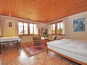 A room with a wooden ceiling, a bed, a desk with chairs, and a bookshelf. - Chalet Bodenweg Appartement/Fewo, Bad, WC, 1 Schlafraum 1-Zimmerwohnung by Interhome (Frutigen)