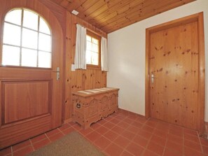 A room with wooden walls and a tiled floor, featuring a large arched window, a wooden dresser, and two wooden doors. - Chalet Bodenweg Appartement/Fewo, Bad, WC, 1 Schlafraum 1-Zimmerwohnung by Interhome (Frutigen)