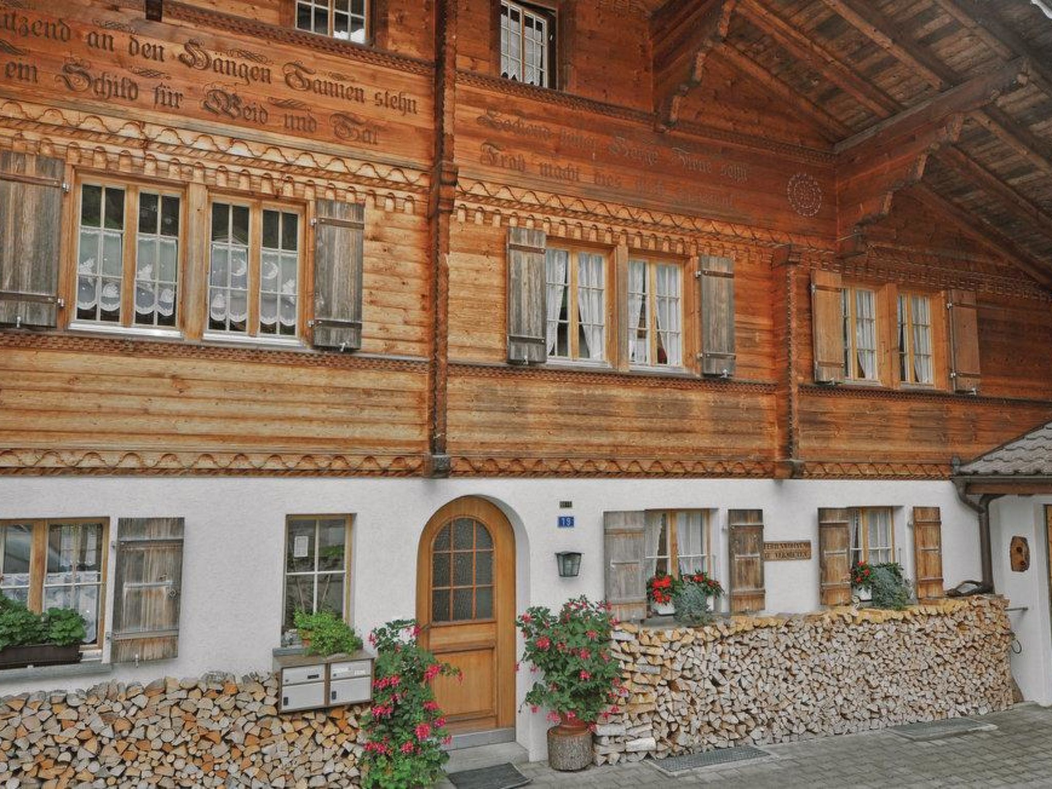A traditional wooden building with multiple windows and a stone wall in front.