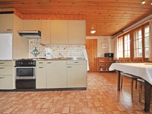 A kitchen with wooden cabinets, a stove, and a dining area with a table. - Chalet Bodenweg Appartement/Fewo, Bad, WC, 1 Schlafraum 1-Zimmerwohnung by Interhome (Frutigen)