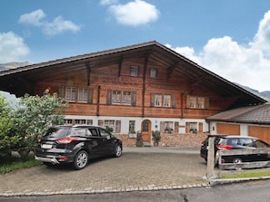 A two-story wooden house with a sloped roof, a paved driveway, and two parked cars. - Chalet Bodenweg Appartement/Fewo, Bad, WC, 1 Schlafraum 1-Zimmerwohnung by Interhome (Frutigen)