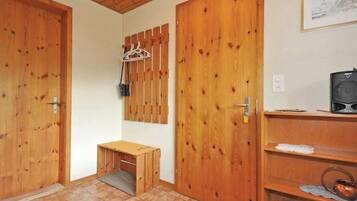 Une pièce avec des portes en bois, un petit banc en bois, une étagère contenant des ustensiles de cuisine et un tableau encadré au mur.
