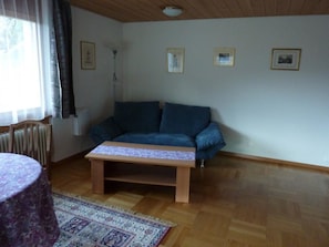 A living room with a sofa, a small table, a patterned rug, and framed pictures on the wall. - Abesunne Appartement/Fewo, Dusche, WC, 1 Schlafraum Sarbach - Erdgeschoss by Interhome (Frutigen)