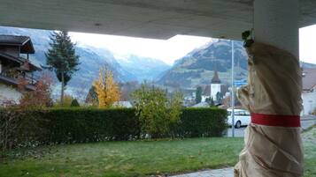 Une statue représentant une personne portant un ruban rouge, surplombant un paysage montagneux avec une église et des immeubles d’habitation.