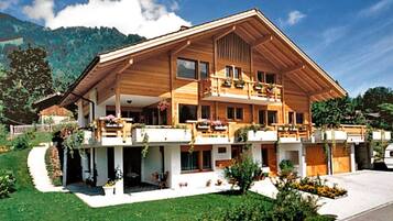 Un chalet en bois à deux étages, doté de balcons, entouré d’un jardin bien entretenu et avec une vue sur les montagnes.