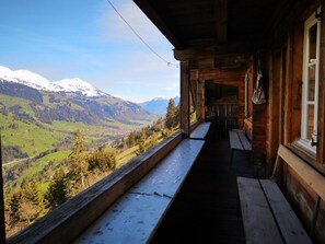 Een houten hut met een balkon met uitzicht op een vallei en besneeuwde bergen.
