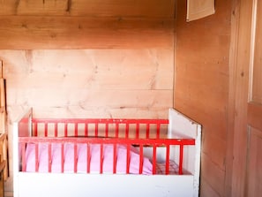 A wooden cabin interior with a single bed featuring a red frame and white bedding.