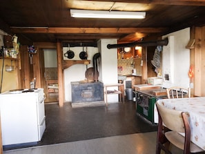 A rustic kitchen with wooden beams, a stove, and a dining table with chairs.