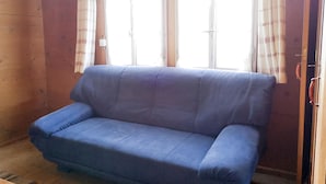 A room with a blue sofa, two windows with curtains, and wooden walls. - Weidhütte Wegscheide Hütte, Dusche, WC, 3 Schlafräume Wohnung 1. Stock by Interhome (Frutigen)