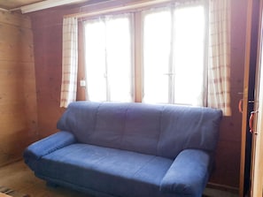 Ein Zimmer mit einem blauen Sofa, zwei mit Vorhängen versehenen Fenstern und Holzwänden.