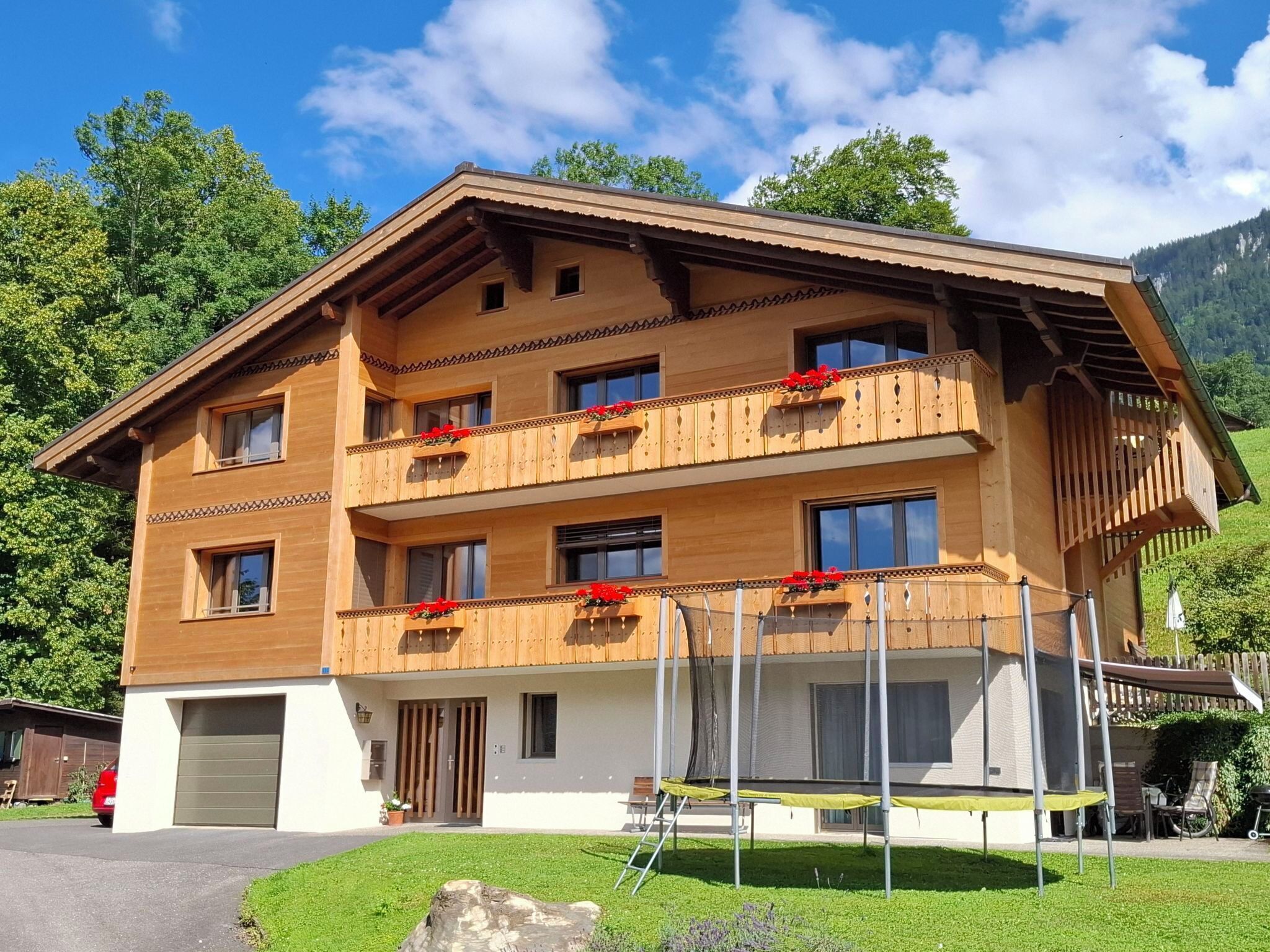 Een chalet met meerdere verdiepingen, balkons, een garage en een berg op de achtergrond.