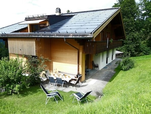 Ein modernes Haus mit Satteldach, einem Essbereich mit Gartenmöbeln und einem Rasen.
