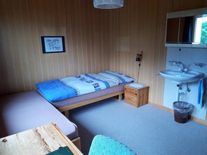 A bedroom with a single bed, a small bedside table, a wooden dresser, a wall-mounted shelf, and a bathroom with a sink and mirror. - Chalet Wenger Appartement/Fewo, Dusche und Bad, WC, Balkon by Interhome (Reichenbach)
