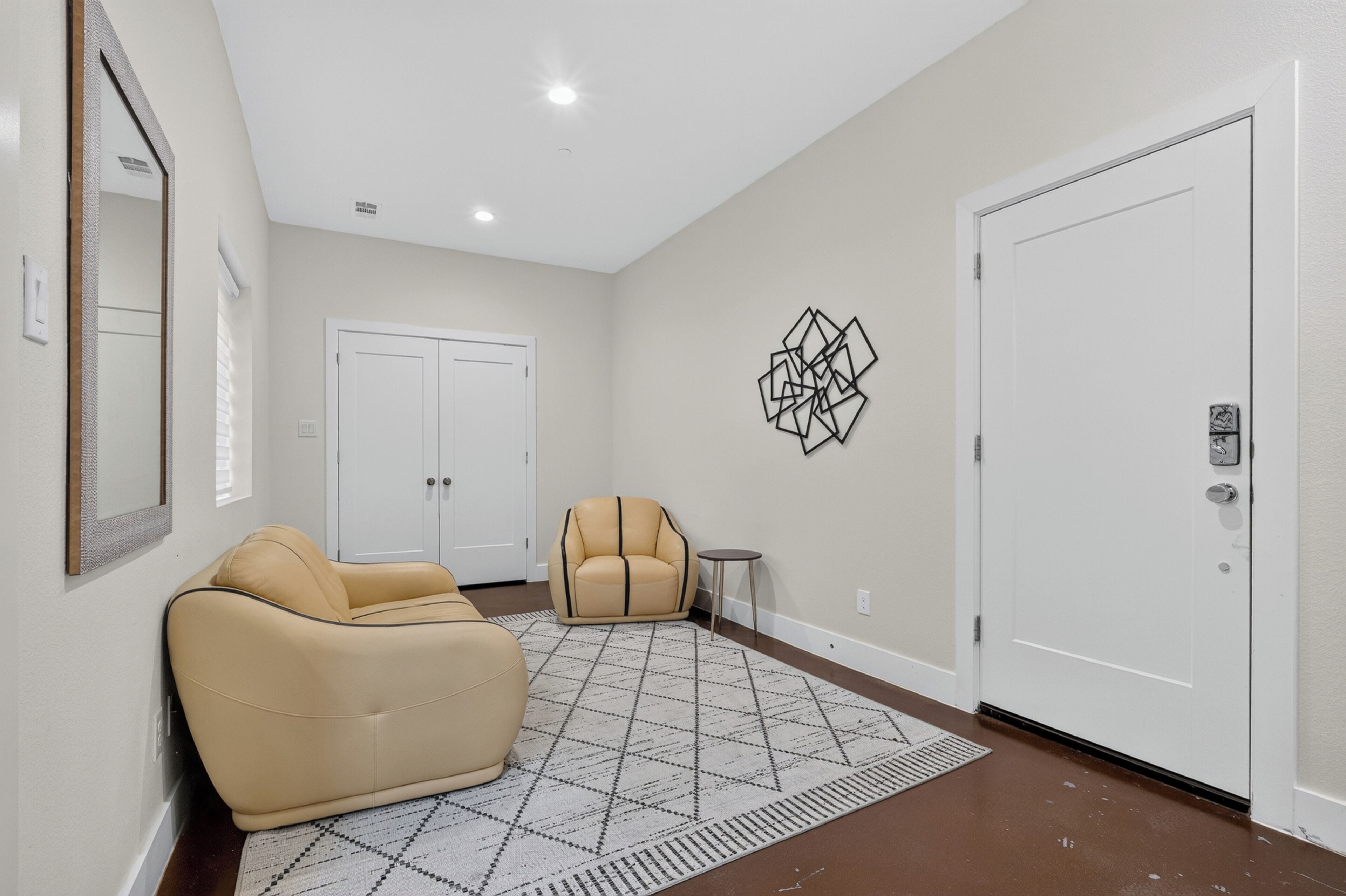 A hallway with a beige sofa, a patterned rug, a door, and a wall-mounted geometric art piece.