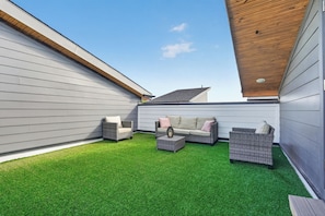 Eine Terrasse mit einer grauen Wand, einer Holzbeschichtung und einem grünen Rasen aus künstlicher Grasnarbe.