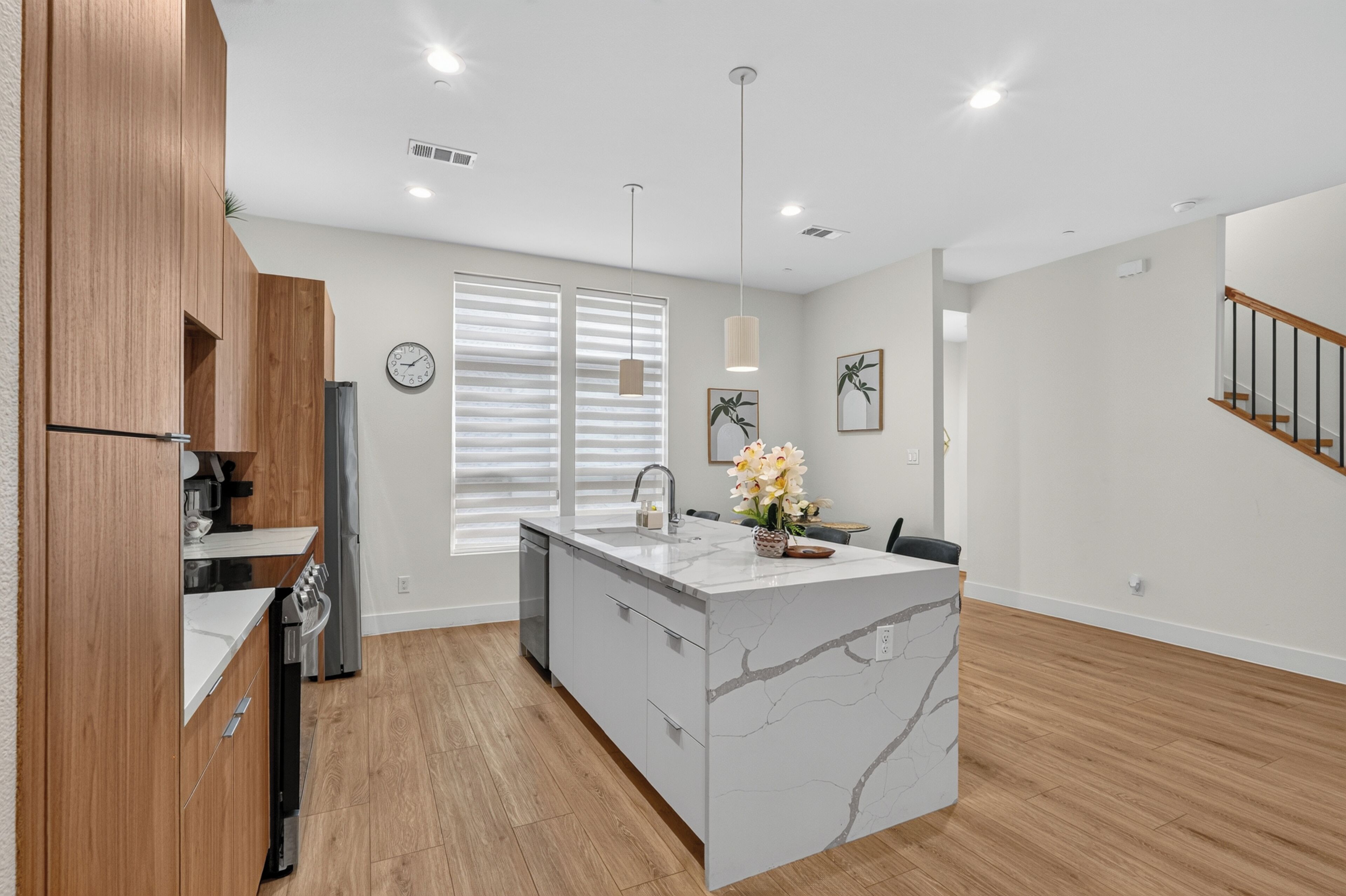 A modern kitchen with a marble island, wooden cabinets, a built-in oven, and a large window with blinds.