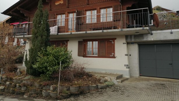 Una casa de campo de dos pisos con balcón, contraventanas de madera y garaje.