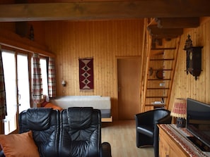 Ein gemütliches Zimmer mit einem Bett, einem Schreibtisch mit Computer, einem Sessel und einer Holzwand.
