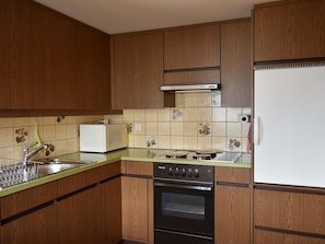 A kitchen with wooden cabinets, a white refrigerator, a stove, and a microwave. - Chalet Niesenblick Appartement/Fewo, Bad, WC, 2 Schlafräume 3-Zimmerwohnung by Interhome (Reichenbach)