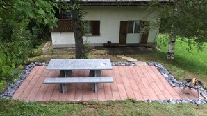 A patio with a stone table and benches, surrounded by a stone border, in front of a house with a white exterior and brown shutters. - Schalmi Appartement/Fewo, Dusche, WC, 2 Schlafräume 3-Zimmerwohnung DG by Interhome (Adelboden)