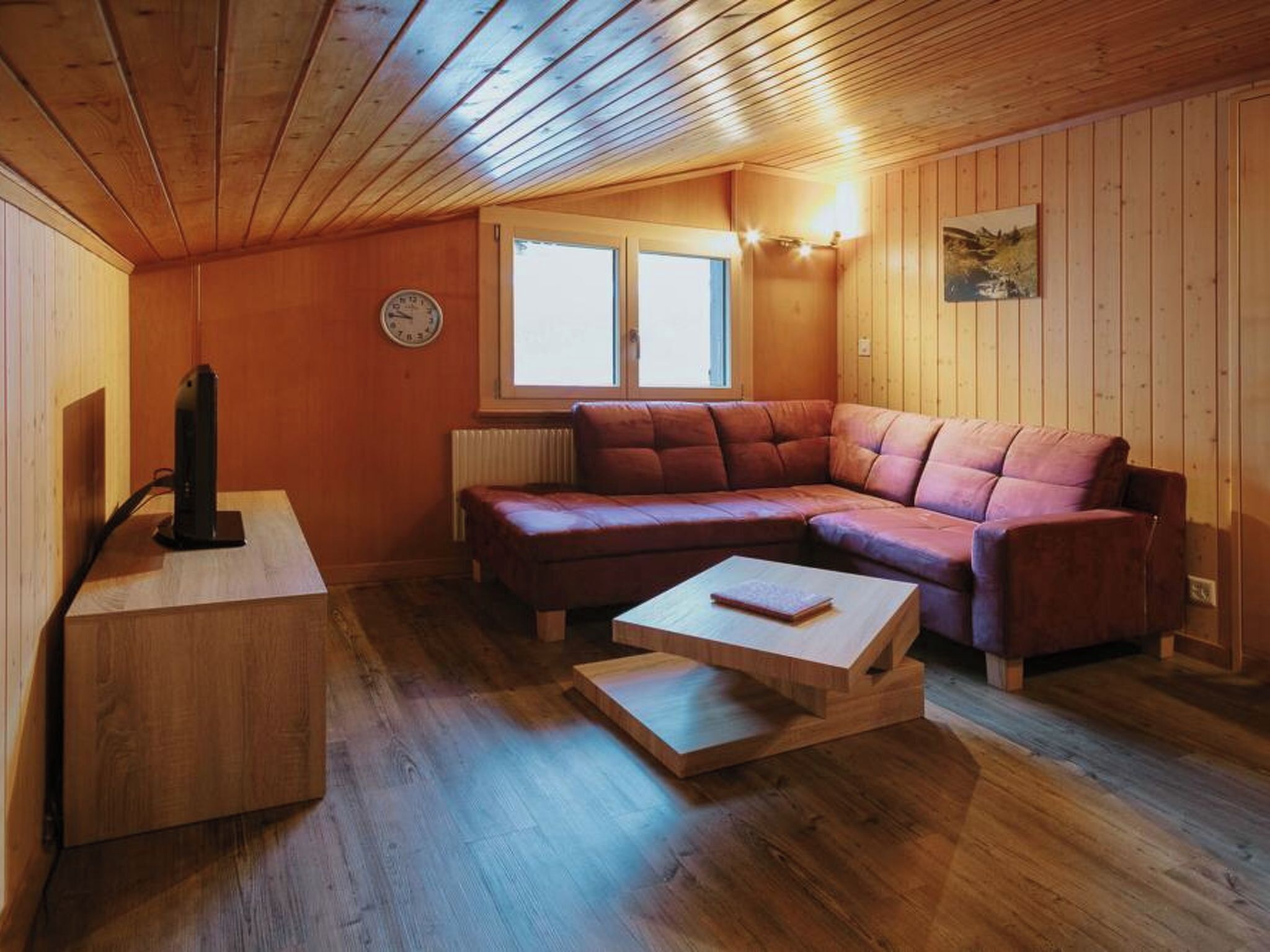 Ein gemütliches Zimmer mit Holzbalkendecke, einem roten Ledersofa, einem Holztisch und einer Heizung.