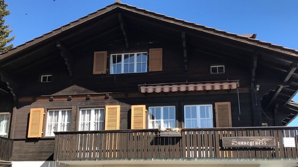 Ein zweistöckiges Gebäude mit einem Balkon, Holzhörnern und einem Schild mit der Aufschrift 'Sunness'.