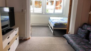 Ein kleines Zimmer mit Bett, Sofa, Fernseher und Heizkörper.