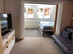 Ein kleines Zimmer mit Bett, Sofa, Fernseher und Heizkörper.
