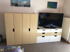 A room with a television on a stand, a wardrobe with multiple doors, and a radiator. - Sunnegruess UG Appartement/Fewo, Dusche, WC 1.5 Zimmerwohnung by Interhome (Adelboden)