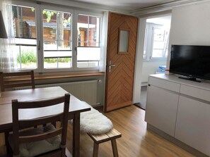 A room with a dining table, chairs, a television, and a door leading to an outdoor area. - Sunnegruess UG Appartement/Fewo, Dusche, WC 1.5 Zimmerwohnung by Interhome (Adelboden)