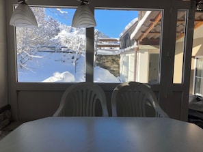 Ein Essbereich mit Tisch und Stühlen, ein Fenster mit Blick auf eine verschneite Landschaft und einer Lampe.
