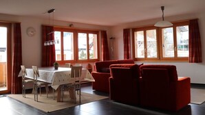 En stue med en rød sofa, et spisebord med stole og store vinduer.
