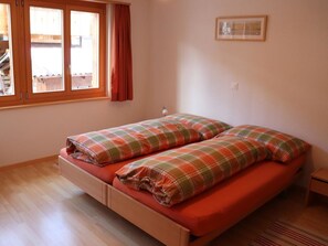 A bedroom with a wooden bed, two pillows, a window with curtains, and a wall-mounted picture. - Liimerweg Appartement/Fewo, Bad, WC, 2 Schlafräume 3.5-Zimmerwohnung by Interhome (Adelboden)