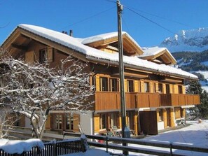 Eine zweistöckige Holzhütte mit Balkon, umgeben von schneebedeckten Bäumen und Bergen.