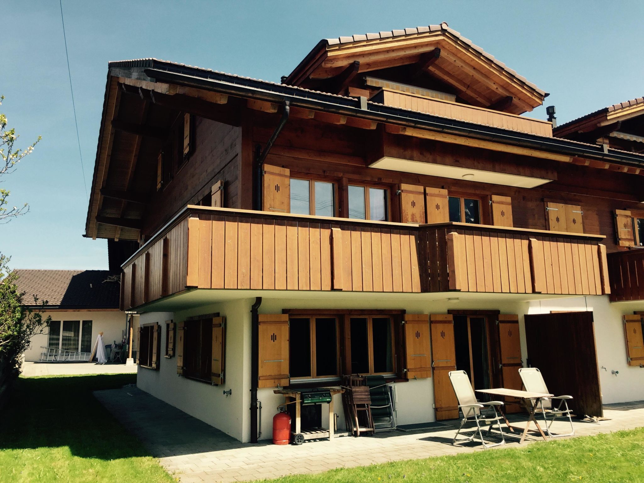 Ein zweistöckiges Holzhaus mit Balkon, Grillplatz und Garage.