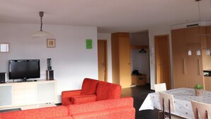 En stue med fjernsyn, sofa og spiseområde med et bord.