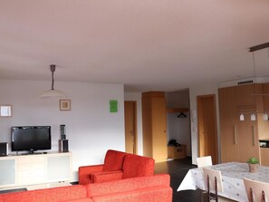 Ein Wohnzimmer mit Fernseher, einer Couch und einem Essbereich mit Tisch.