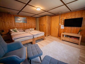 Ein Zimmer mit einem Bett, einem Fernseher, einem Schreibtisch und einem Sessel.