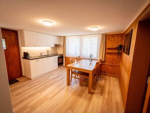 A compact kitchen with wooden cabinets, a dining table, and a window with curtains. - Trachsels Heimetli Appartement/Fewo, Dusche, WC, 1 Schlafraum 2-Zimmer-Wohnung by Interhome (Kandergrund)